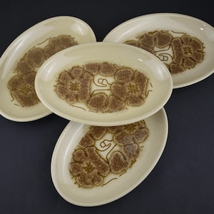 May include: Four oval serving platters. The plates have a cream base with a brown floral design in the centre. The floral design is surrounded by a brown outline. The plates are stacked on top of each other.