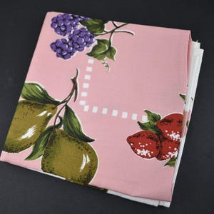 May include: A folded fabric square featuring a light pink background with a repeating pattern of purple blackberries, green pears with leaves, and red strawberries. A white dashed square border is printed in the centre of the fabric.