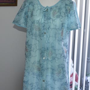 May include: A pale blue vintage nightdress with a floral design. The nightdress features short sleeves, a tie at the neckline, and buttons down the front. The fabric is sheer and lightweight, suitable for sleepwear.
