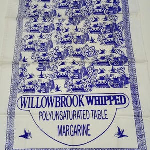 May include: A white kitchen towel with a blue Willowbrook Whipped Polyunsaturated Table Margarine design. The towel has a repeating pattern of blue houses, trees, and birds. The words "WILLOWBROOK WHIPPED POLYUNSATURATED TABLE MARGARINE" are printed in blue.