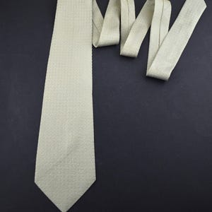 May include: A light green tie with a subtle textured pattern. The tie is displayed against a dark background, showcasing its color and design. The tie is a classic accessory for formal or business attire.