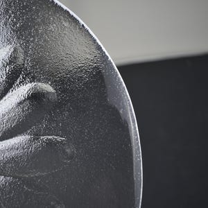 May include: A clear glass plate featuring a raised, textured floral design on its underside. The embossed pattern depicts a central flower with numerous radiating petals, creating a tactile surface that catches the light across the circular edge.