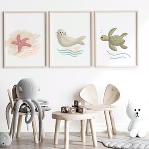 Three separate framed illustrations of a sea turtle, starfish and a seal hanging on the wall on a child’s playroom with toys