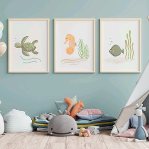 Three separate framed illustrations of a sea turtle, sea horse and a fish hanging on the wall on a child’s playroom with toys