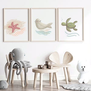 Illustration of sea turtle, seal and a star fish in wood frames hung on a white wall in a child’s room with toys
