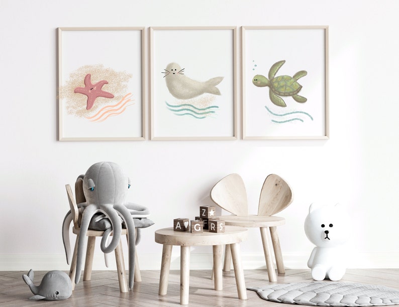 Illustration of sea turtle, seal and a star fish in wood frames hung on a white wall in a child’s room with toys