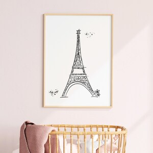 Black and white Eiffel Tower line drawing in frame in pink nursery above a crib