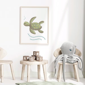 Illustration of sea turtle nursery art in a wood frame hung on a white wall in a children’s playroom with toys