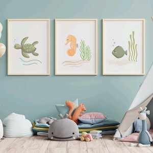 Illustration of sea turtle, sea horse, and fish wood frames hung on a blue wall in a child’s playroom with toys