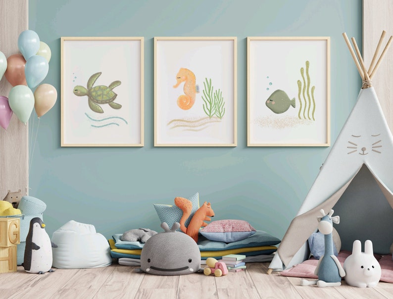 Illustration of sea turtle, sea horse, and fish wood frames hung on a blue wall in a child’s playroom with toys