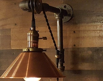 May include: A copper-toned industrial style wall lamp with a pulley system and a black cord. The lamp has a copper-toned shade and a brass socket.