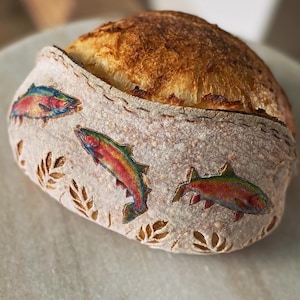 May include: A sourdough bread loaf with a crusty exterior and a soft interior. The loaf is decorated with colourful fish designs.
