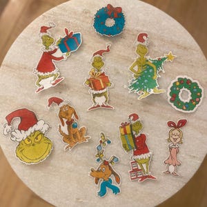 May include: A set of nine Christmas-themed stickers featuring the Grinch and other characters from the popular holiday film. The stickers are printed on a white background and feature a variety of festive designs, including a Christmas tree, a wreath, and a gift.