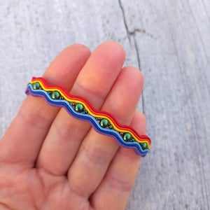 Op de afbeelding: Een regenboogkleurige armband met groene kralen. De armband is gemaakt van een golvend, elastisch materiaal.