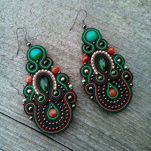 May include: A pair of green and brown earrings with intricate beadwork and a teardrop shape. The earrings feature a green gemstone and brown beads.