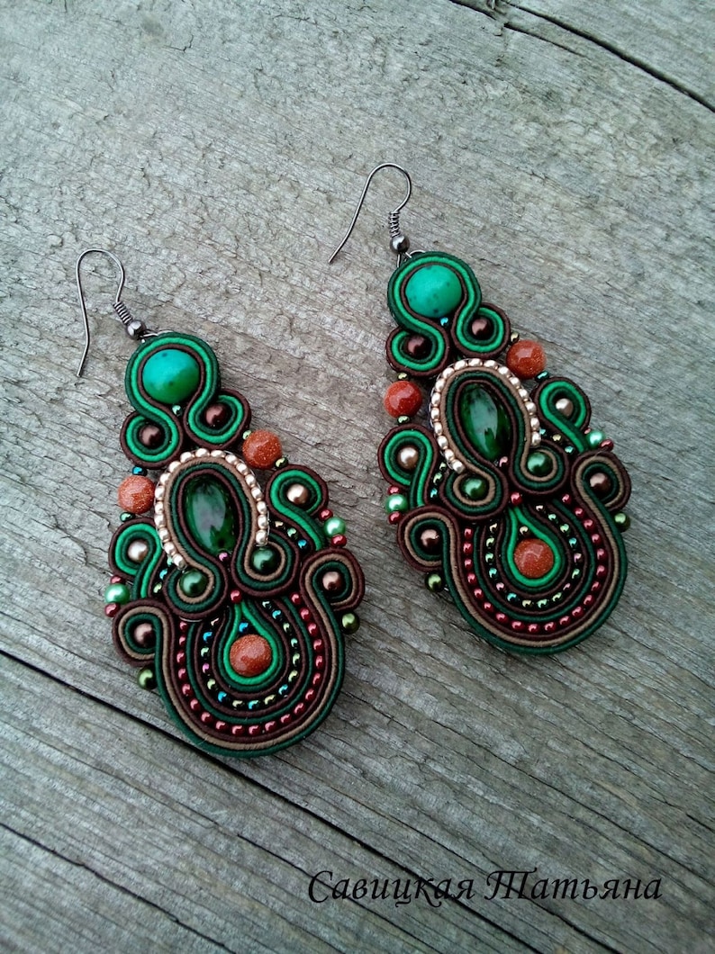 May include: A pair of green and brown earrings with intricate beadwork and a teardrop shape. The earrings feature a green gemstone and brown beads.
