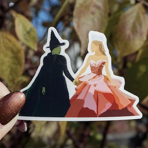May include: A sticker featuring a silhouette of two women, one in a green witch costume and the other in a pink and red ball gown. They are holding hands and facing each other.