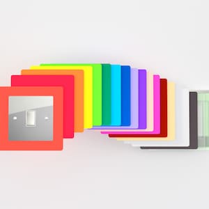 May include: A set of light switch covers in a rainbow of colours, including red, orange, yellow, green, blue, purple, pink, and white. The covers are made of plastic and have a glossy finish.