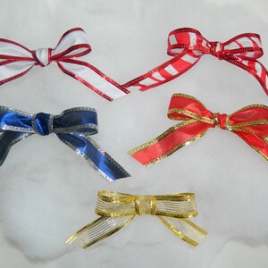 May include: Four different ribbon bows in various colors and patterns. The bows are made of satin ribbon with a silver trim. The bows are arranged in a row on a white background.