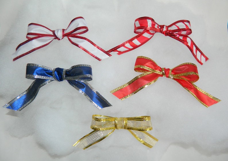 May include: Four different ribbon bows in various colors and patterns. The bows are made of satin ribbon with a silver trim. The bows are arranged in a row on a white background.