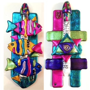May include: A colorful mezuzah with a Star of David design and three fish. The mezuzah is made of painted wood and has a turquoise background. The fish are pink, yellow, and blue with silver and gold accents.
