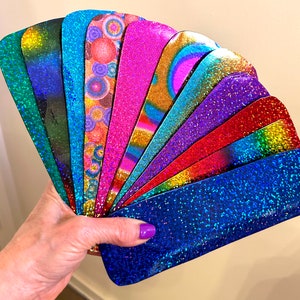 May include: A fan of 10 different iridescent glitter cardstock sheets in various colours, including blue, green, purple, pink, and red.