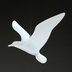 Peut inclure: Une sculpture d'oiseau en céramique blanche suspendue au plafond. L'oiseau est en vol, les ailes déployées.