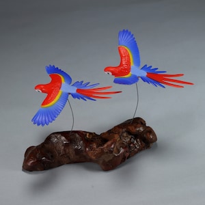 Könnte beinhalten: Zwei rote und blaue Aras, die auf einem Holzast sitzen. Die Aras sind im Flug mit ausgebreiteten Flügeln. Der Holzast ist braun und hat eine raue Textur.