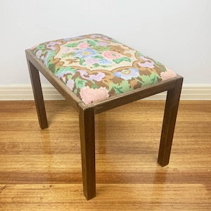May include: A small wooden stool with a floral patterned cushion. The cushion has a brown background with pink, green, and blue flowers.