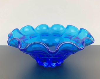 Könnte beinhalten: Eine blaue Glasschüssel mit einem gewellten Rand und einem strukturierten Boden. Die Schüssel ist aus klarem Glas und hat einen hellblauen Farbton.