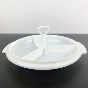 Puede incluir: Plato de servir de plástico blanco con tres secciones divididas y un asa. El plato es redondo y tiene un borde elevado.
