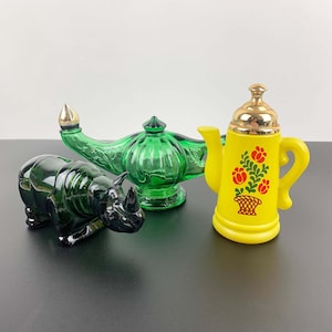Puede incluir: Tres botellas de perfume vintage de vidrio. Una lámpara de genio verde, un rinoceronte negro y una tetera amarilla con diseño floral rojo.
