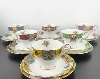 May include: A collection of vintage teacups and saucers. Each teacup features a unique tartan pattern in colors like yellow, red, and blue, with gold trim. The saucers match the teacups, creating a cohesive set. The teacups have a classic, elegant design.
