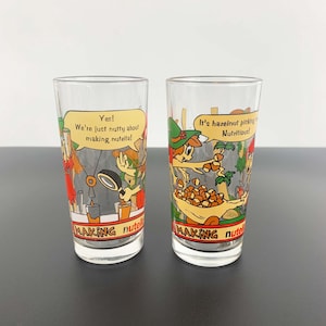 May include: Two clear glass drinking glasses with colorful cartoon illustrations of characters making Nutella. The text on the glasses reads "Yes! We're just nutty about making Nutella!" and "It's hazelnut picking Nutritious!"