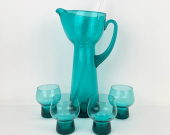 May include: A set of four teal blue glass tumblers and a matching pitcher with a glass straw. The pitcher has a wide mouth and a tall, slender body.