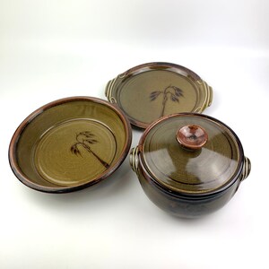 May include: A set of three ceramic dishes with a brown and green glaze. The dishes feature a stylised tree design. The set includes a large platter, a smaller bowl, and a covered casserole dish.