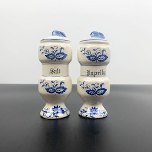 Może przedstawiać: Zestaw dwóch vintage ceramicznych solniczek i pieprzniczek z niebiesko-białym wzorem kwiatowym. Solniczki są oznaczone jako "Sól" i "Papryka".
