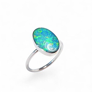 May include: A silver ring featuring an oval opal gemstone. The opal displays a vibrant mix of blue, green, and yellow hues. The ring has a simple, elegant design with a polished finish, suitable for everyday wear.
