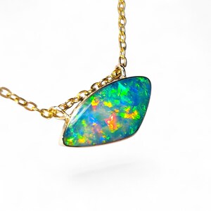 May include: A gold chain necklace featuring a marquise-shaped opal pendant. The opal displays a vibrant play-of-color with flashes of neon green, electric blue, and warm orange tones set within a polished gold bezel frame on a delicate link chain.