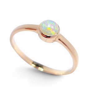 Peut inclure: Une bague en or rose ornée d'une opale ronde et irisée. L'opale présente un jeu de couleurs, notamment du vert, du jaune et du bleu. La bague a un anneau délicat et un design simple et élégant.