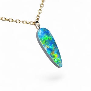May include: A gold chain necklace featuring a pendant. The pendant is an elongated, teardrop-shaped opal displaying vivid blue, green, and yellow colours. The opal is set against a white backdrop.