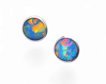 Puede incluir: Un par de pendientes de ópalo redondos. Cada pendiente presenta una vibrante piedra de ópalo multicolor engastada en un bisel plateado. Los ópalos muestran una mezcla de azules, verdes, naranjas y amarillos, creando un efecto brillante.