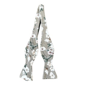 May include: A beige bow tie with a white floral pattern. The bow tie has a green stem and leaf design.