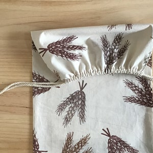 May include: A white cotton drawstring bag with a brown wheat pattern. The bag has a white drawstring and is made of natural fabric.