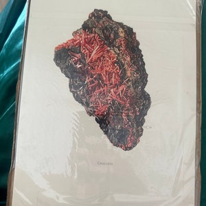 Könnte beinhalten: Eine Nahaufnahme eines roten und schwarzen Crocoit-Mineralien-Exemplars. Das Mineral hat eine raue, strukturierte Oberfläche und wird auf weißem Hintergrund gezeigt.