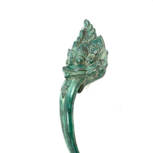 May include: A green metal door handle with a decorative design of a mythical creature's head.