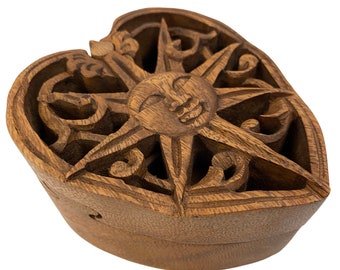 May include: A heart-shaped wooden box with intricate carvings of a sun face and floral designs. The box is made of dark brown wood and has a lid that opens to reveal the interior.