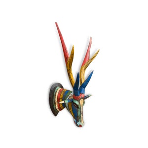 May include: A colorful, hand-painted wooden deer head wall decor. The antlers are red, yellow, and blue. The head features a mix of blue, green, and white paint with striped details. The deer head is mounted on a black wooden base.