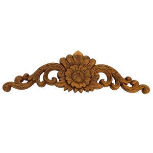 May include: A carved wooden floral design with intricate details. The design features a large flower in the center with smaller floral motifs on either side. The wood is a rich brown color.