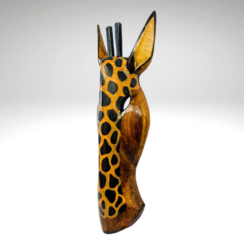 May include: Wooden giraffe mask with a brown base and black and orange painted spots. The mask has a long neck and large ears.